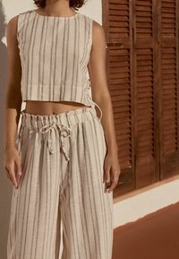 Ensemble léger en lin composé de deux pièces : un haut court à rayures verticales et un pantalon taille haute à jambes larges avec une ceinture à cordon.