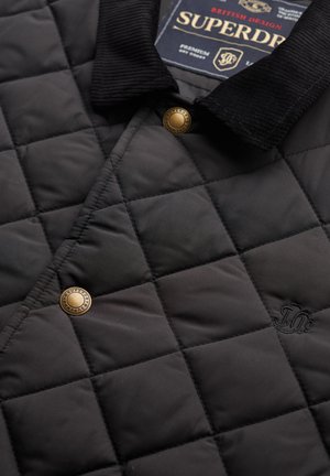 Sort quilted jakke med en kordfløjlskrave, med gyldne trykknapper og broderede detaljer. Materialet ser glat og holdbart ud.
