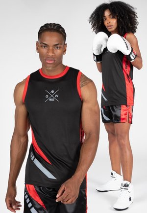 Zwarte sportieve tanktop met rode accenten en grijze strepen, gecombineerd met zwarte shorts met rode bies en grafische afbeeldingen, gedragen met witte boksbandages.
