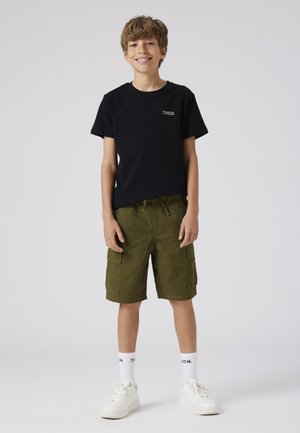T-shirt nera in cotone con logo "TWSN", pantaloni cargo verdi con tasche laterali, calzini bianchi e sneakers bianche su uno sfondo neutro.