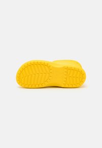Une chaussure Crocs jaune vif montrée depuis la semelle, mettant en valeur le motif de texture de la semelle et le logo de la marque au centre.