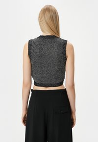 Top grigio cropped senza maniche con un motivo a maglia testurizzato e orlo a costine in contrasto. Indossato con pantaloni neri a vita alta con tasca laterale.