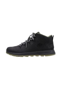 Zapatillas de senderismo de media altura negras con cordones grises, suela de goma y un cuello acolchado verde; presenta un logo en el lateral y detalles texturizados.