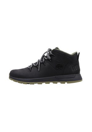 Zapatillas de senderismo de media altura negras con cordones grises, suela de goma y un cuello acolchado verde; presenta un logo en el lateral y detalles texturizados.