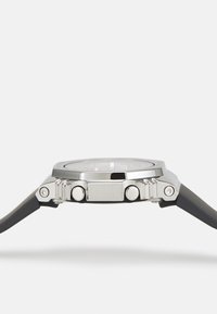 Montre en acier inoxydable argenté avec un boîtier rond, un bracelet en caoutchouc et deux boutons sur le côté. La surface en verre est lisse et claire.