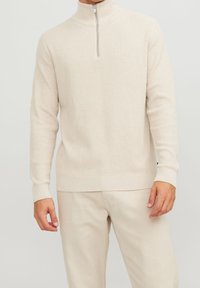 Beige zip-necktröja i strukturerad stickning med långa ärmar och en figurnära nederkant. Kombineras med ljusa byxor.