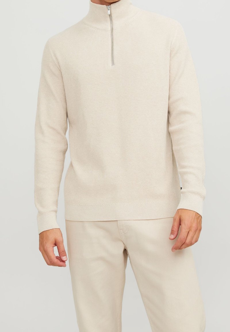 Beige zip-necktröja i strukturerad stickning med långa ärmar och en figurnära nederkant. Kombineras med ljusa byxor.