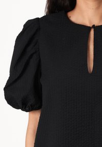 Black dress with textured fabric, short puff sleeves, and a small keyhole neckline detail. Designed for a relaxed fit.