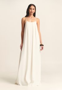 Robe maxi blanche fluide avec des fines bretelles, design plissé et texture douce. Notable pour son tissu léger et son style minimaliste.