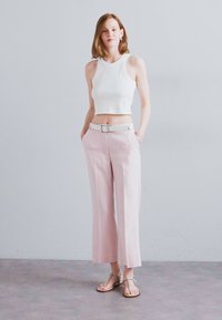 Top de tip cropped alb, pantaloni roz deschis cu picioare largi și curea, și sandale plate. Țesătură netedă, design minimalist, fundal neutru.