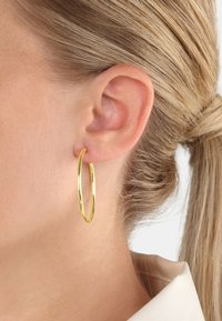 Pendiente de aro de oro, de tamaño mediano, con forma ovalada y superficie brillante, exhibido en un lóbulos de oreja, con una textura suave y mínimos acentos.