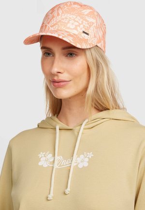 Marhuľová šiltovka s kvetinovým vzorom, vybavená zahnutým šiltom a štítkom na boku. Nosená s béžovou mikinou s kapucňou, ktorá má bielu logo.