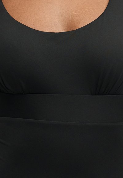 Κοντινό πλάνο ενός ατόμου που φοράει μαύρο αμάνικο τοπ με φαρδύ ντεκολτέ και εφαρμοστή λεπτομέρεια στη μέση.