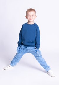 Niebieska bluza z prążkowanym dekoltem, zestawiona z jasnoniebieskimi, farbowanymi metodą tie-dye spodniami cargo z kieszeniami oraz białymi trampkami.