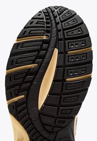 Shoe sole tread in black with gold accents, featuring textured geometric patterns and grooves designed for traction and flexibility.