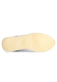 Semelle d'une chaussure avec une surface texturée en caoutchouc de couleur blanc cassé, comportant des nervures pour l'adhérence et une zone de bout lisse pour la flexibilité.