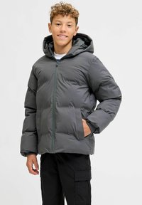 Giacca imbottita grigia con cappuccio, dotata di cerniera frontale, tasche laterali e polsini a coste. Texture liscia con pannelli trapuntati.