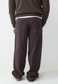 Donkerpaarse wijde broek van katoen, met twee achterzakken en een relaxte pasvorm. De tailleband zit boven de heupen.