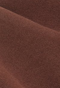 Brun texturerad tyg med en mjuk, fluffig yta som ser skiktad ut och har en enhetlig färg utan mönster eller detaljer.