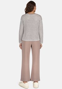 Jasnoszary sweter z dzianiny o teksturowym wzorze, zestawiony z jasnoróżowymi spodniami o szerokich nogawkach i białymi trampkami, widoczny z tyłu.