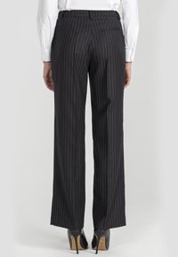 Czarne spodnie w prążki o prostym kroju, z paskiem w talii i subtelnymi detalami na tylnych kieszeniach, zestawione z czarnymi szpilkami.
