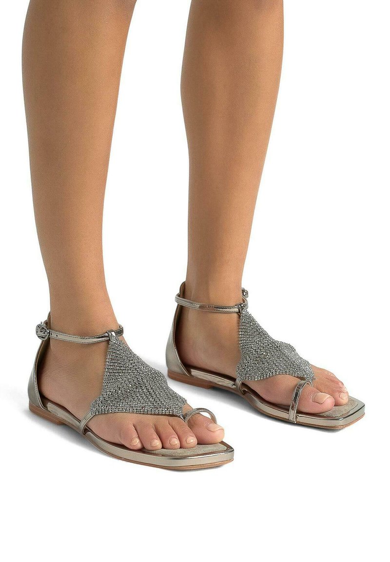Sandali piatti con cinturini metallici silver e dettagli in rete scintillante intricati. Design open-toe e fibbia alla caviglia per una vestibilità sicura.