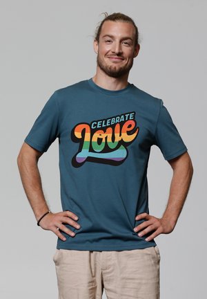 Teal cotton T-shirt featuring a colorful graphic that reads "Celebrate Love" in orange, yellow, green, and blue text. Short sleeves, relaxed fit.