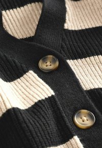 Schwarz-weiße gestreifte Strickjacke mit geripptem Textur, einem V-Ausschnitt und einem großen, runden Knopf am Ausschnitt.