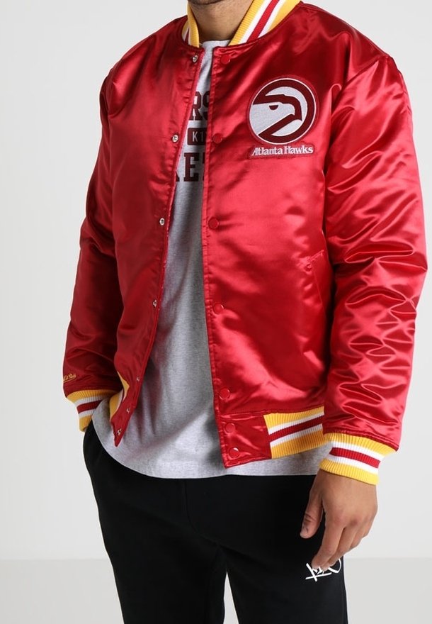 Červená saténová bomber bunda se žlutými a bílými proužkovanými žebrovanými manžetami a límcem. Na levé straně hrudníku je logo Atlanta Hawks.