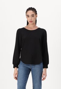 Svart langermet topp med rund hals og samlet mansjett, kombinert med blå jeans. Glatt stoff med en avslappet fasong.