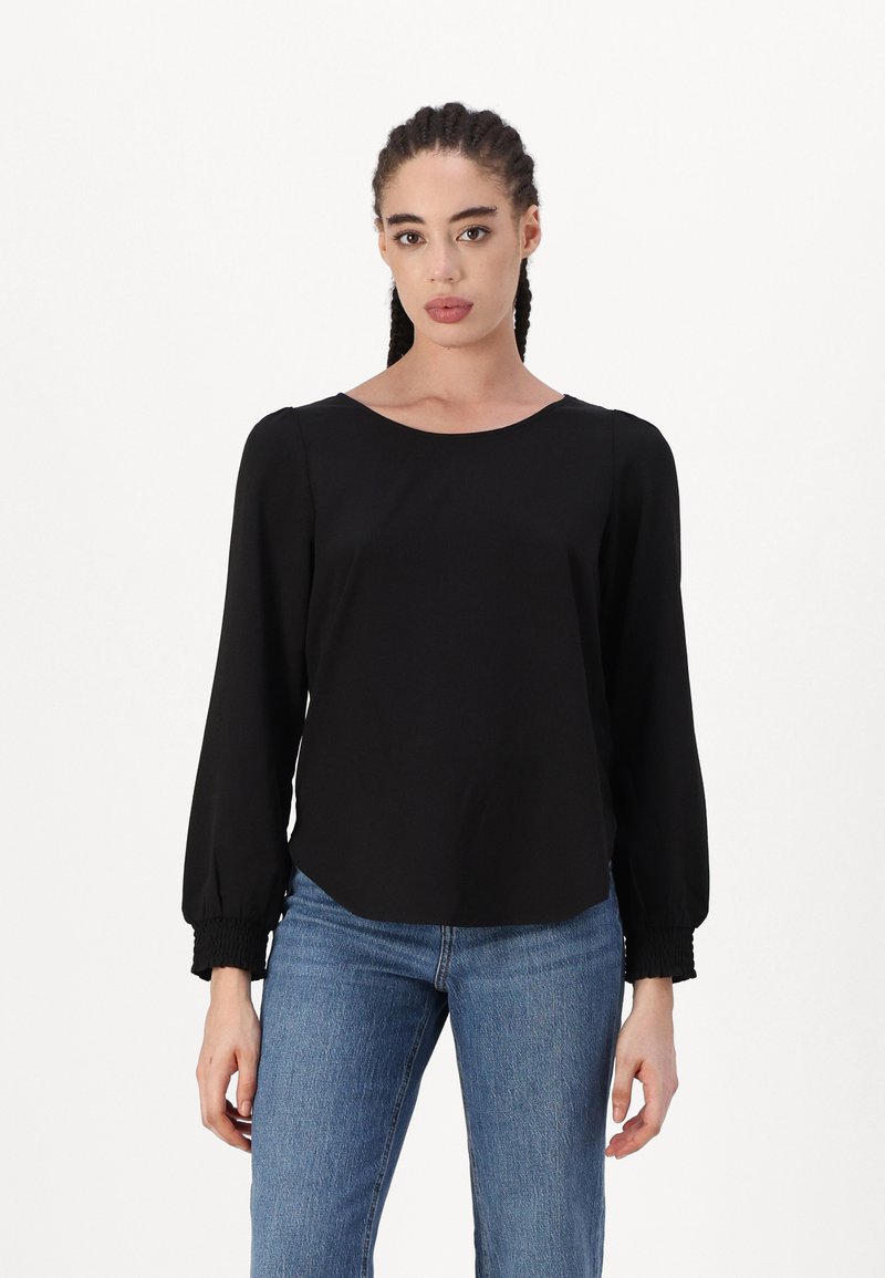 Svart langermet topp med rund hals og samlet mansjett, kombinert med blå jeans. Glatt stoff med en avslappet fasong.