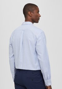 Camicia a maniche lunghe a righe blu e bianche, realizzata in tessuto leggero, con piega sul retro e dettagli a bottoni sui polsini.
