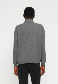 Veste en chevrons grise avec un col montant, des poignets et un ourlet côtelés. Caractérisée par un tissu texturé et une coupe droite et ajustée.