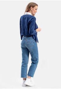 Navyblauw suède cropped jack met lange mouwen, gecombineerd met lichtblauwe rechte jeans en witte sneakers. Het jack heeft een zachte textuur.