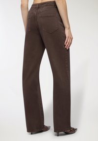 Brązowe spodnie z szerokimi nogawkami, wykonane z miękkiego denimu o gładkiej fakturze, z dwoma tylkimi kieszeniami i średnim stanem.