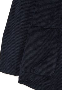 Tessuto di velluto a coste blu scuro con trama a costine verticali, caratterizzato da una grande tasca frontale. I bordi sono rifiniti con un orlo pulito e uniforme.