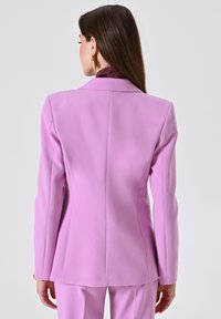 Op maat gemaakte blazer in lichtroze stof met een gestructureerde pasvorm. Voorzien van een klassieke kraag en een gladde textuur, ontworpen voor een professionele uitstraling.