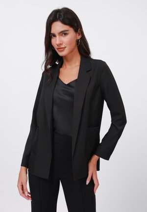 Black blazer with a tailored design, two front pockets, and open lapels. Worn over a black satin top, featuring a smooth texture.