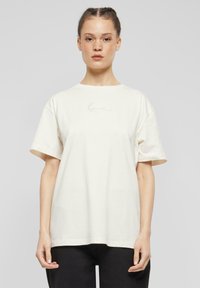 Cremefarvet bomulds-t-shirt med rund halsudskæring og korte ærmer. Har et diskret, broderet logo i lys rosa på brystet.
