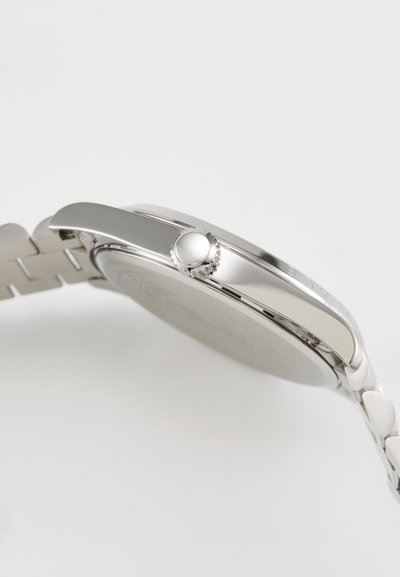 Montre en acier inoxydable argenté avec un boîtier lisse et rond, une couronne texturée et un bracelet à maillons de forme ovale.