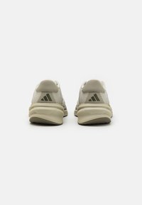 Weiße Sportschuhe mit einem strukturierten_mesh-Obermaterial, beige Akzenten und grüner Markenkennzeichnung. Die Ferse verfügt über eine erhöhte Rückseite und ein stromlinienförmiges Design.