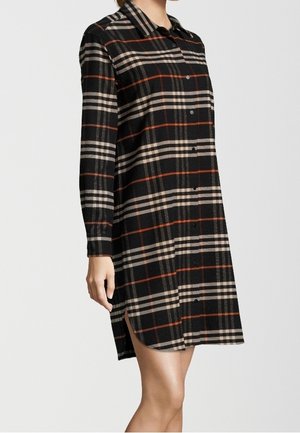 Czarna, beżowa i rdzawa długa koszulowa sukienka w kratę z kołnierzykiem, guzikami z przodu i rozcięciem po boku noszona przez stojącą osobę.