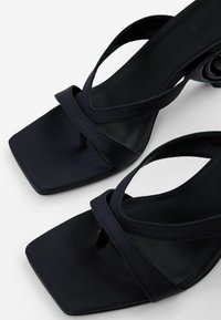Schwarze, geschnallte Absatzsandalen mit quadratischer Spitze, die überkreuzte Riemen und eine glatte, matte Oberfläche verfügen. Elegantes und minimales Design.