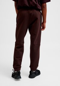 Brune atletikbukser med elastisk talje, indsnævret ben og sort lynlåslomme-detalje. Bruges med sorte atletiksko.