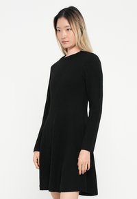 Vestido negro de manga larga con escote redondeado, hecho de una tela suave, con un corte de falda acampanada y textura lisa, diseñado para una silueta ajustada.