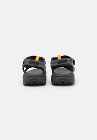 Sandales noires avec des sangles ajustables bleues et un accent orange. Semelle intérieure texturée et semelle en caoutchouc pour l'adhérence. Design à dos ouvert.