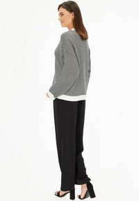 Czarny i biały sweter w zygzaku z białym wykończeniem, połączony z czarnymi szerokimi spodniami i sandałami na blokowym obcasie. Gładkie tekstury.