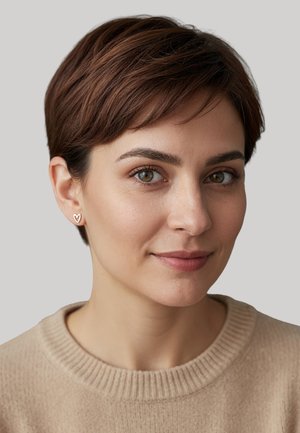 Orecchini a forma di cuore in oro, capelli corti castani, pelle chiara, indossando un maglione beige a collo rotondo con una texture a costine. Sfondo neutro.