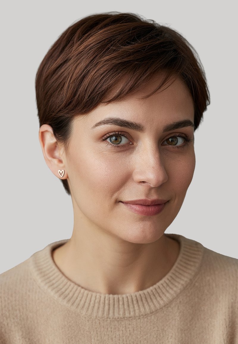 Boucles d'oreilles en forme de cœur doré, cheveux bruns courts, peau claire, portant un pull beige à col rond avec une texture côtelée. Fond neutre.