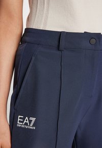 Jūras spēku bikses ar gludu tekstūru, aprīkotas ar pogu aizdari, sānu kabatām un baltu EA7 Emporio Armani logotipu augšstilbā.